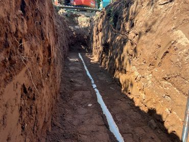 Narrow dirt trench with a white pipe running along the bottom between tall earth walls