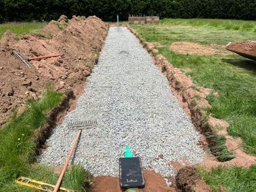 Gravel path under construction beside a lawn, with dirt piles and tools along the edges.