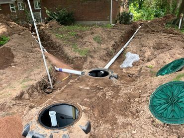 Backyard excavation with three round utility pits, exposed pipes, and dirt mounds around a house