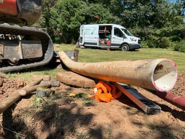 Cylindrical metal pipe on the ground at a work site, with an excavator and white van in the background.