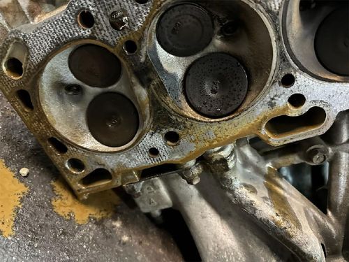 Close-up of a corroded engine cylinder head with carbon buildup and rust stains