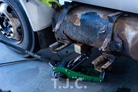 Car on a green floor jack, showing rusted undercarriage and rear wheel in a garage