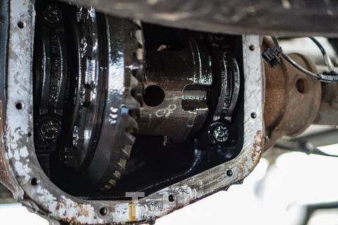 Close-up of an exposed automotive differential or gearbox with gears, bolts, and dark lubricant visible inside.