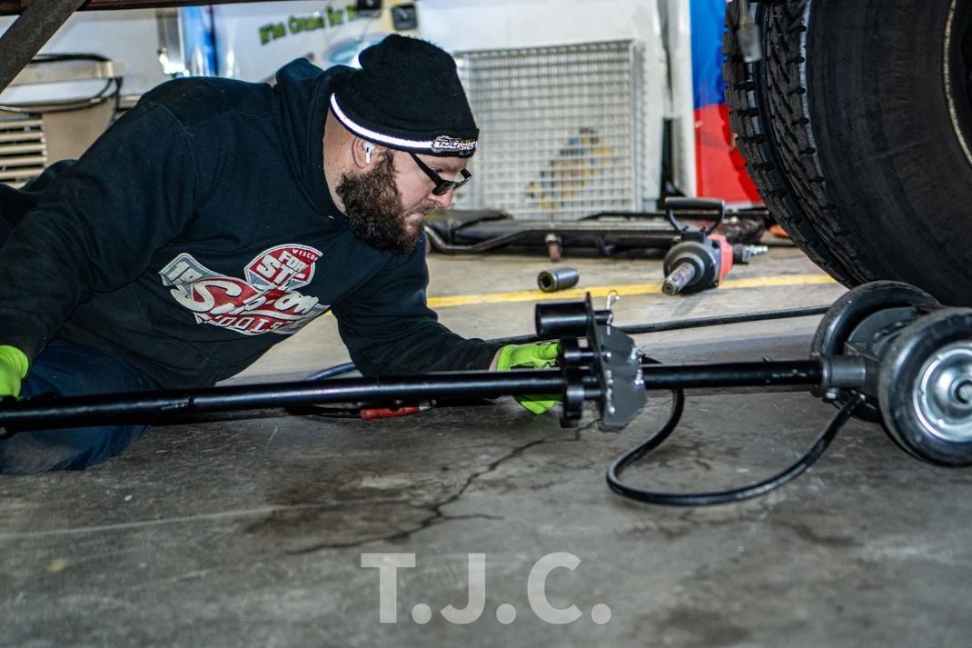 Man in black hoodie using a jack under a car in a garage work area