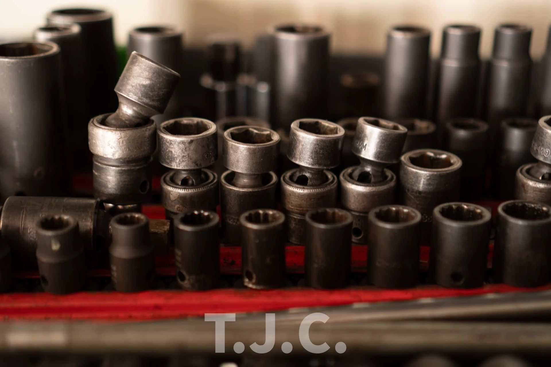 Stack of metal socket wrench heads on a red surface, with blurred tools in the background