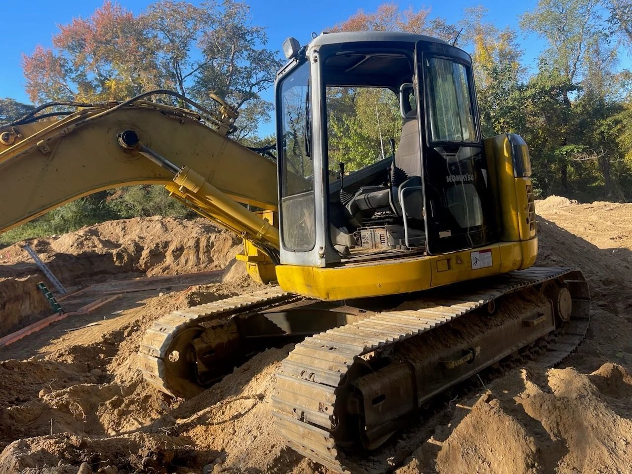 Yellow excavator on tracks digging in a dirt construction site under a blue sky.