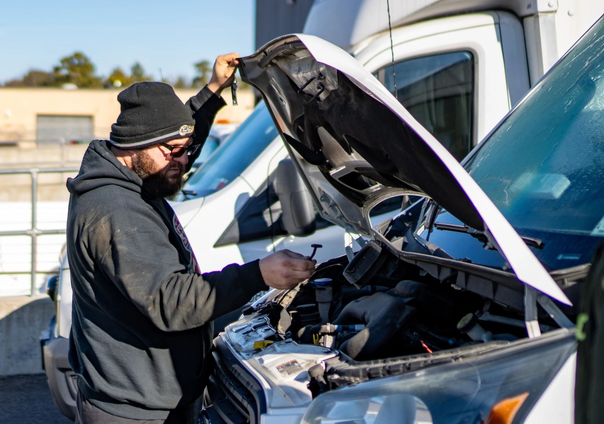 Mechanic inspecting an open van hood outdoors beside other vehicles