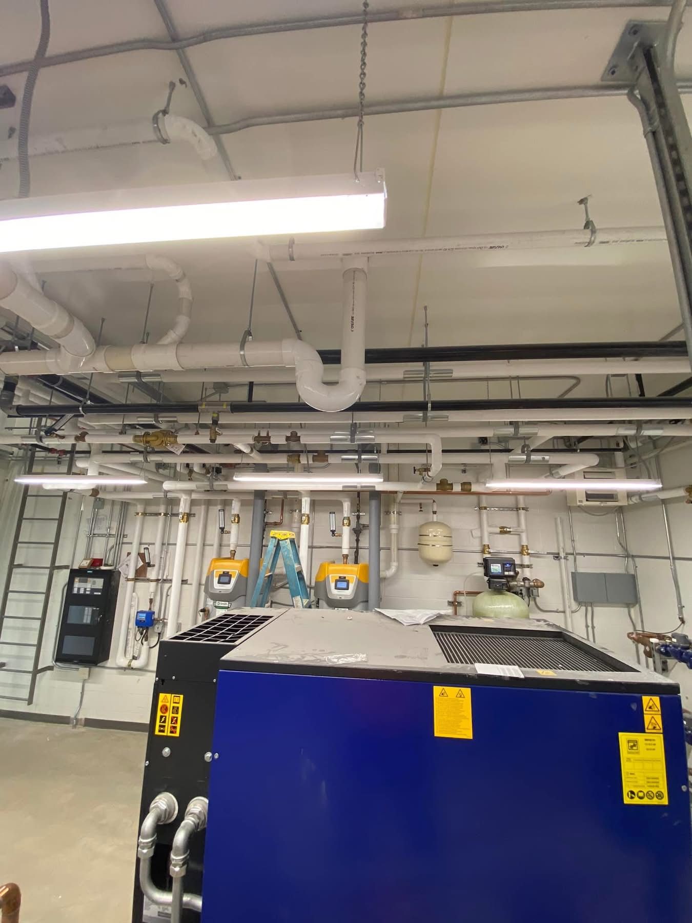 A blue machine is sitting in a room with pipes hanging from the ceiling.