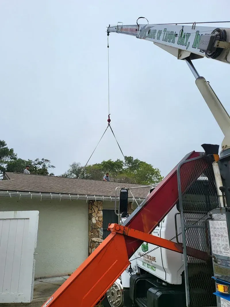 A crane arm extends toward a house roof, with a chain rig suspended from the hook, ready for a lifting operation.