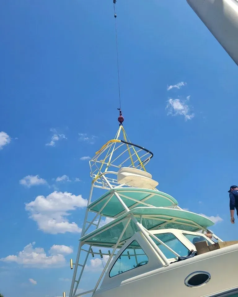 A crane lifts the metal observation tower and roof structure onto the top of a boat under a sunny, blue sky.