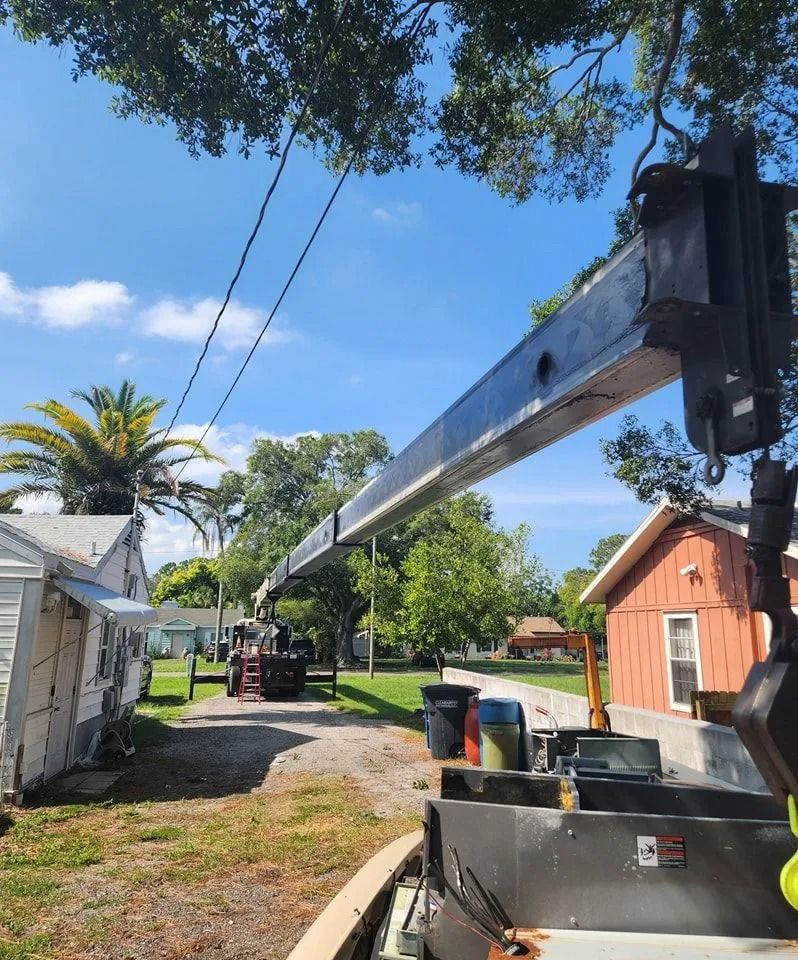 A crane boom extends diagonally across a sunny residential yard between two houses.