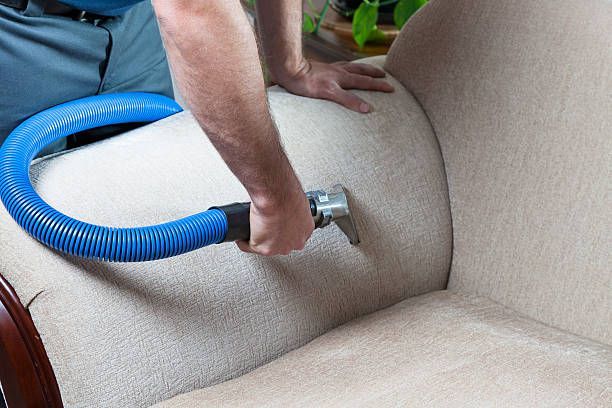 A man is cleaning a couch with a vacuum cleaner.