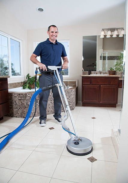 A man is cleaning the floor of a bathroom with a vacuum cleaner.