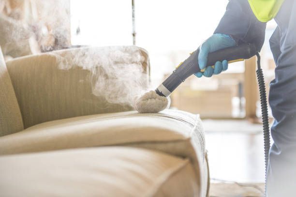 A person is cleaning a couch with a steam cleaner.