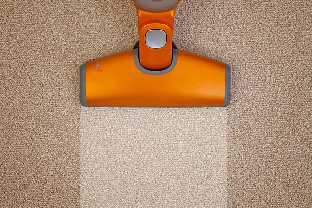 An orange vacuum cleaner is cleaning a carpet.