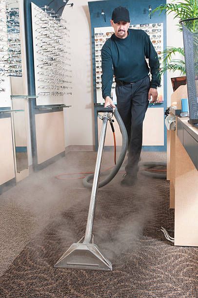 A man is using a vacuum cleaner to clean a carpet in an office.
