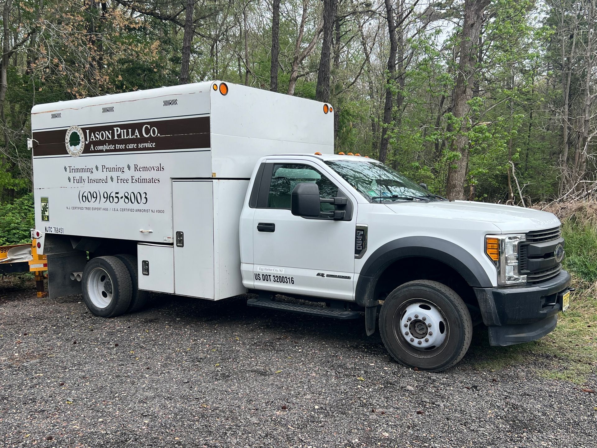 White work truck with a storage box on the back, parked outdoors with trees in the background.