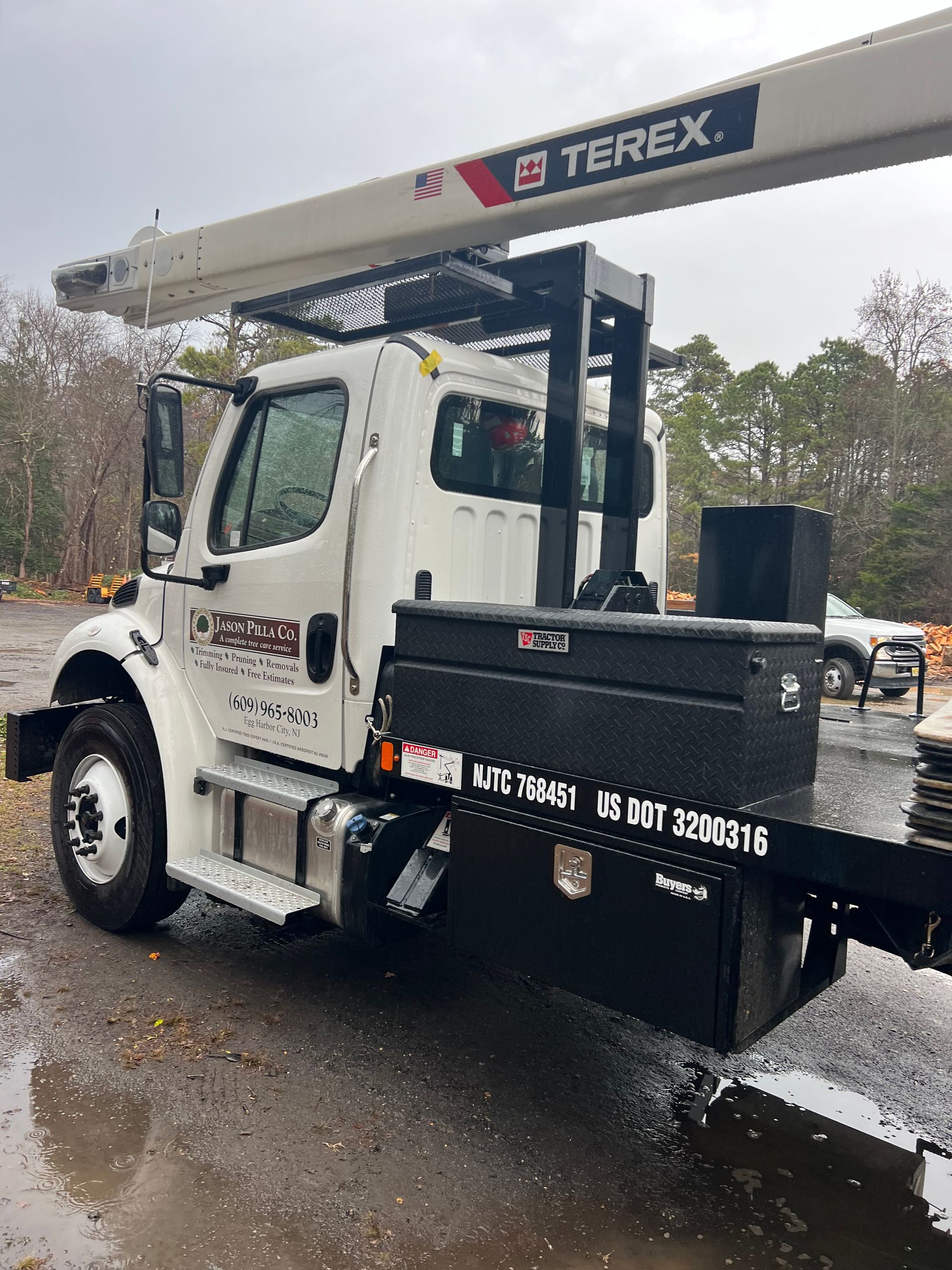 White Terex boom truck with black storage boxes in a wet, outdoor setting.