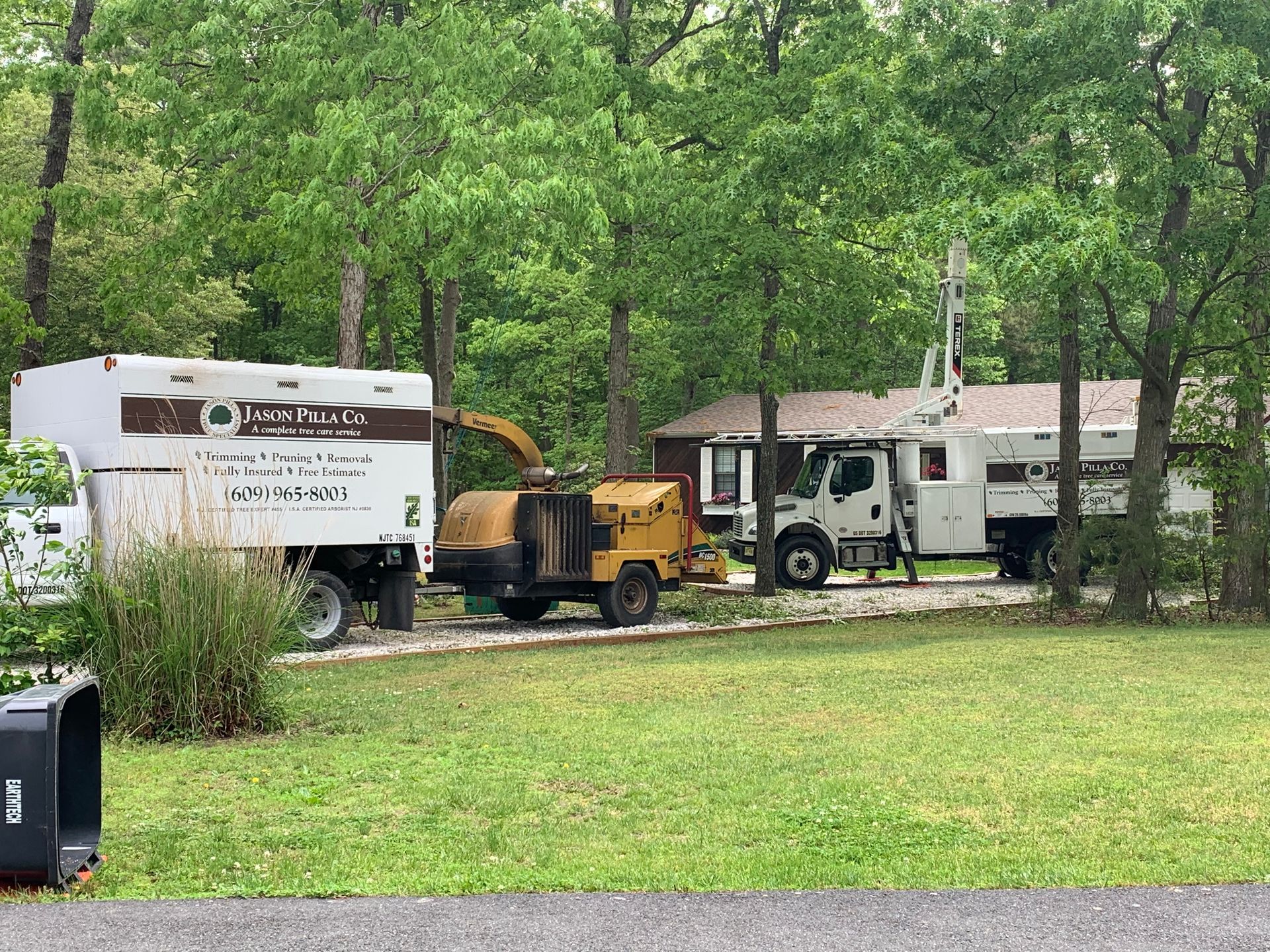 Tree service vehicles parked in front of a house, including a chipper and a truck with a boom.