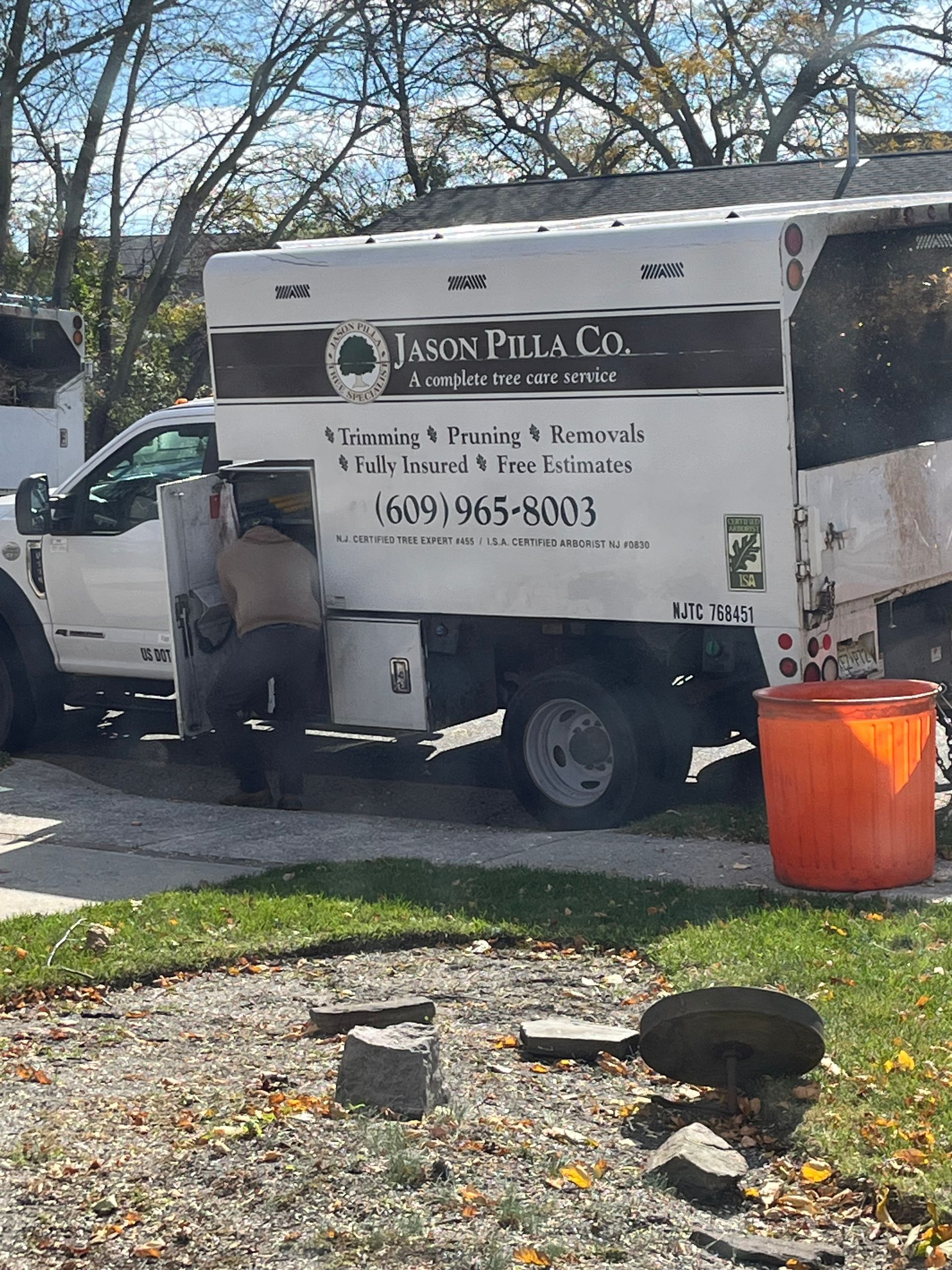 A white Arbor Pillar Co. truck with a person inside; an orange barrel and rocks are in the yard.