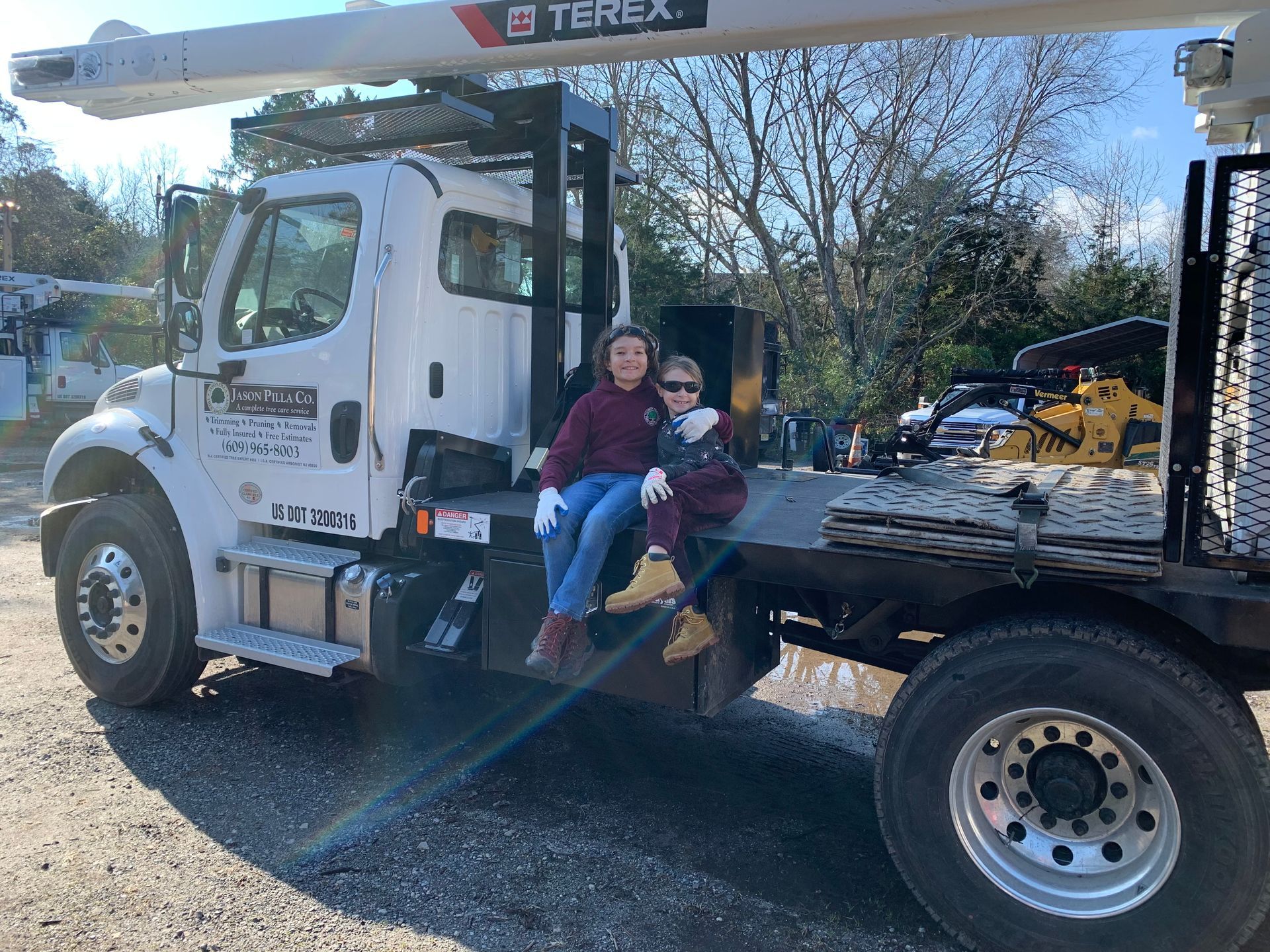 Two people sitting on the back of a white Terex truck. Sunny day.