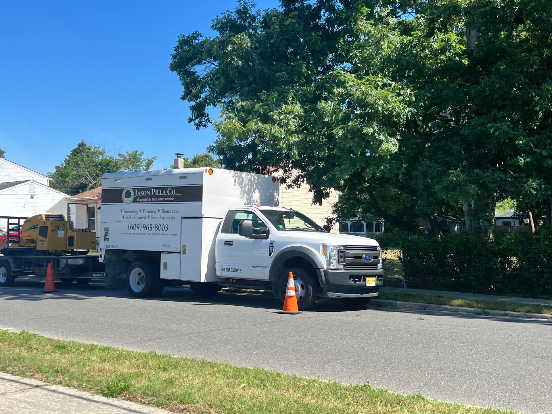 White work truck with a trailer parked on a street near a house; orange traffic cone.
