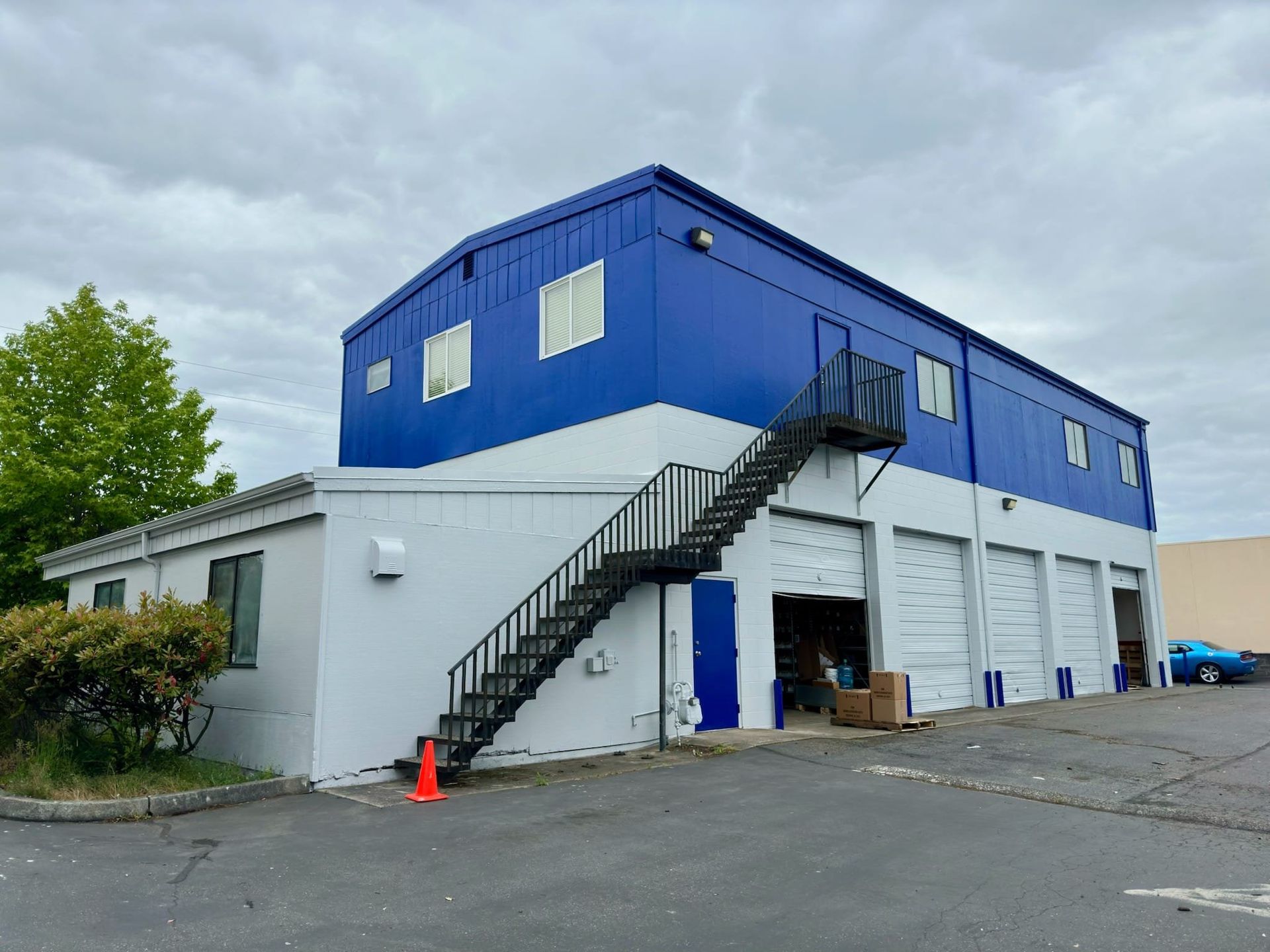 Blue and white industrial building with exterior staircase and garage doors under cloudy sky.