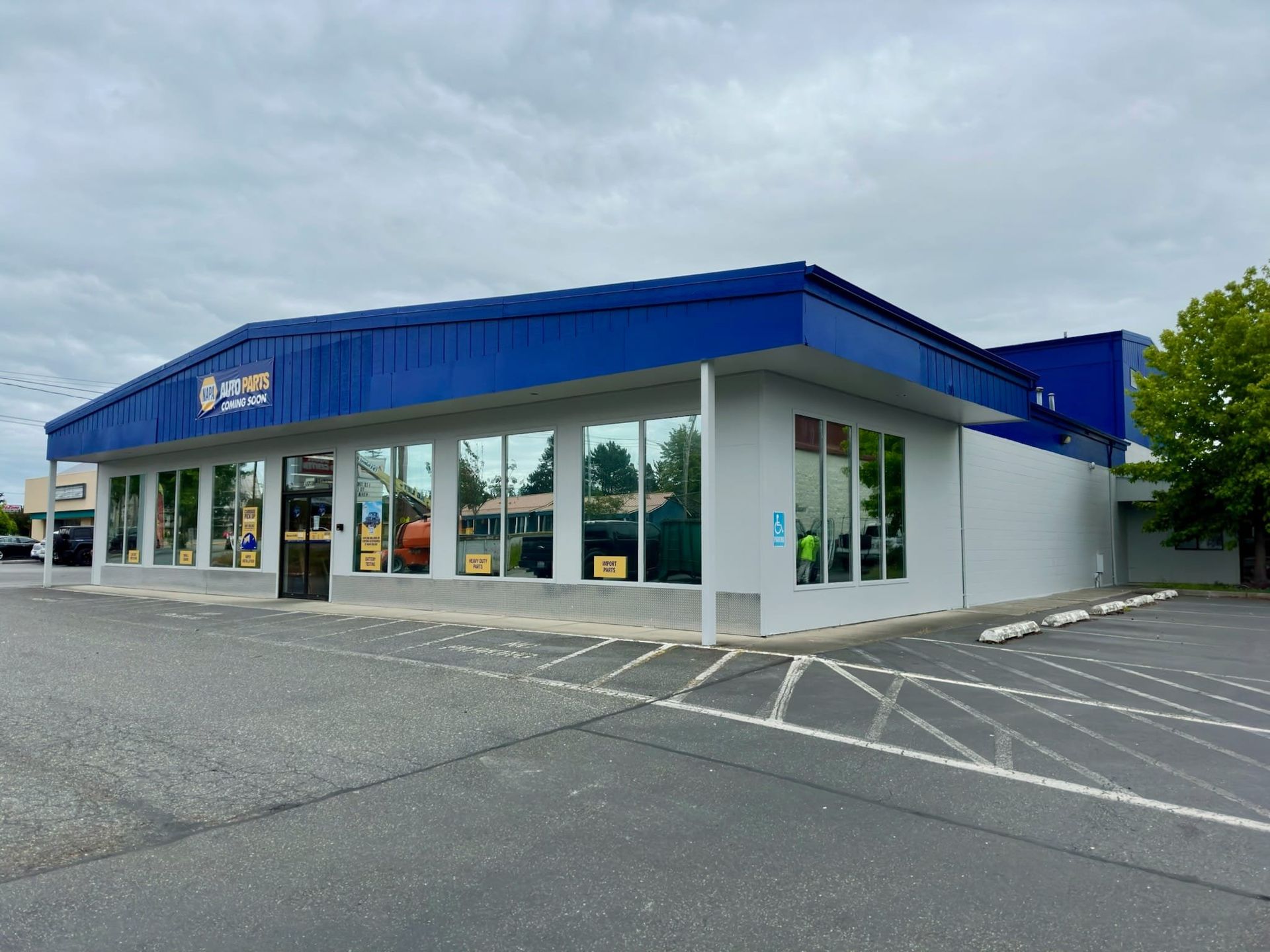 Blue and white auto repair shop with large windows, parking lot, and cloudy sky.
