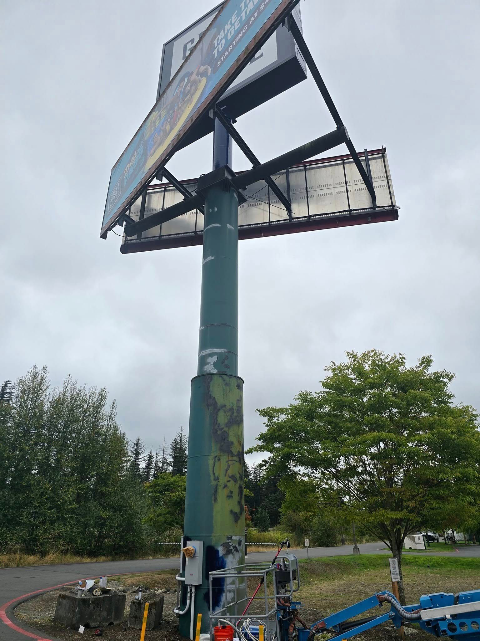 Billboard on a tall green pole; advertisement displays facing away. Overcast sky.