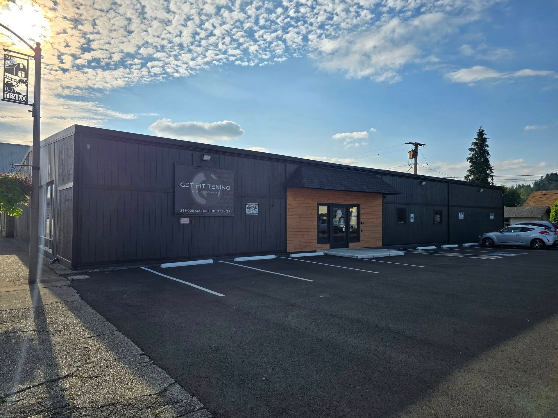 Black building with a wood-paneled entrance, parking lot. Sign says 