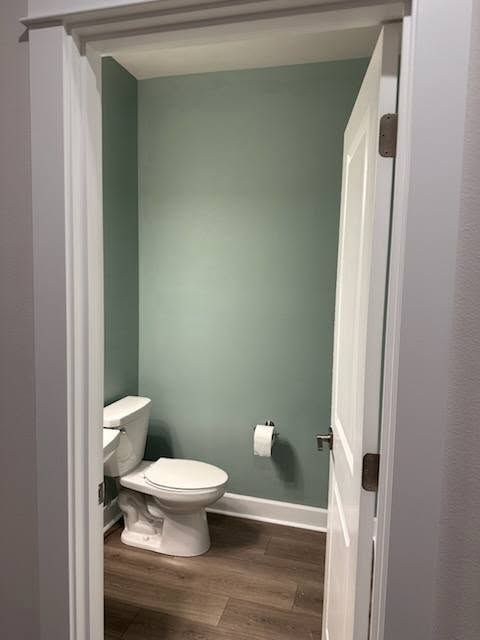 A small powder room with a white toilet, gray-green walls, and a partially open white door.