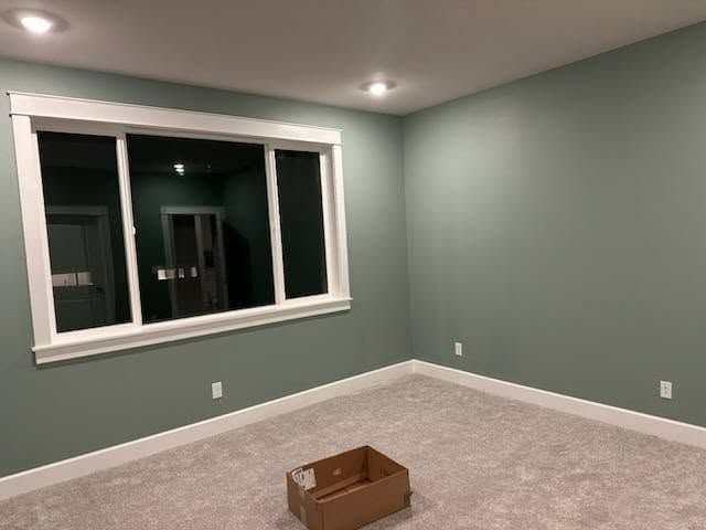 Empty room with green walls, white trim, window, and carpet; cardboard box on floor.