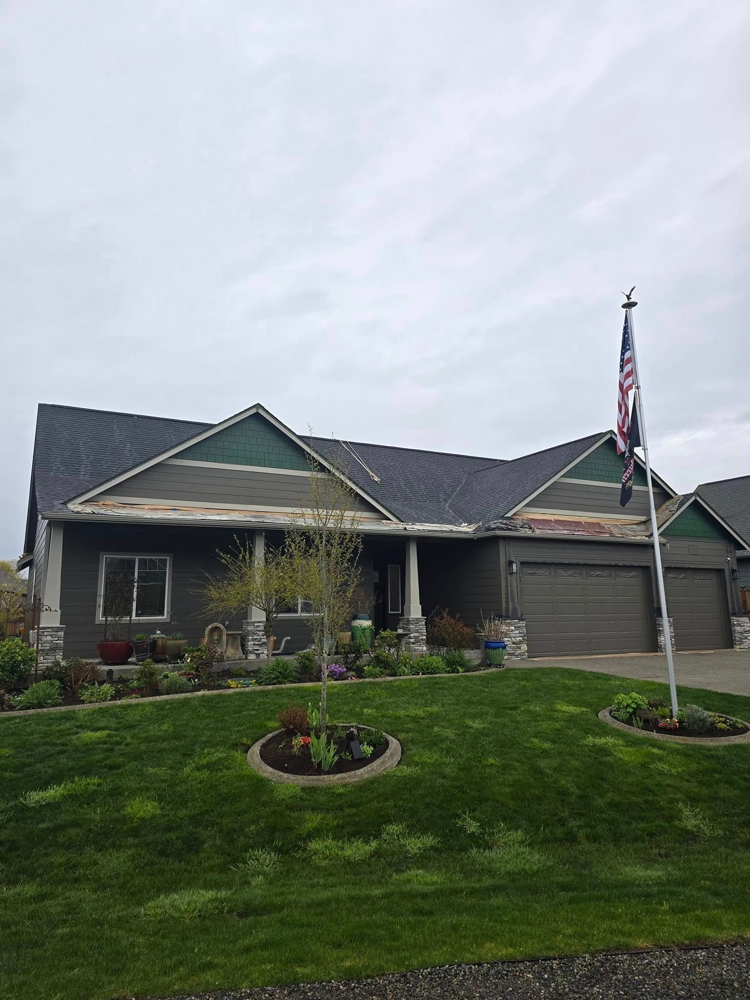 House with green siding and a dark roof, a front yard with grass, and a flagpole flying the US flag.