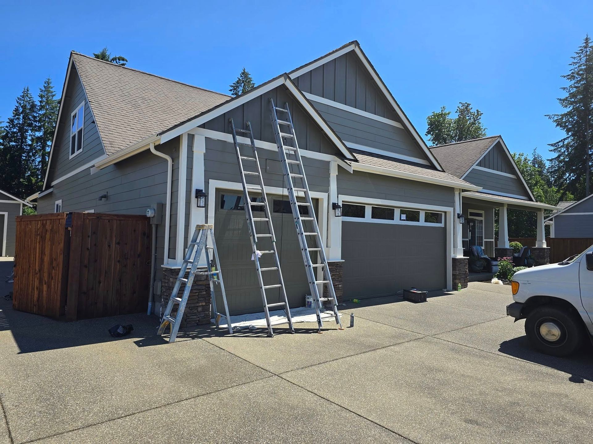 Gray house with ladders leaning against it; truck parked to the right.