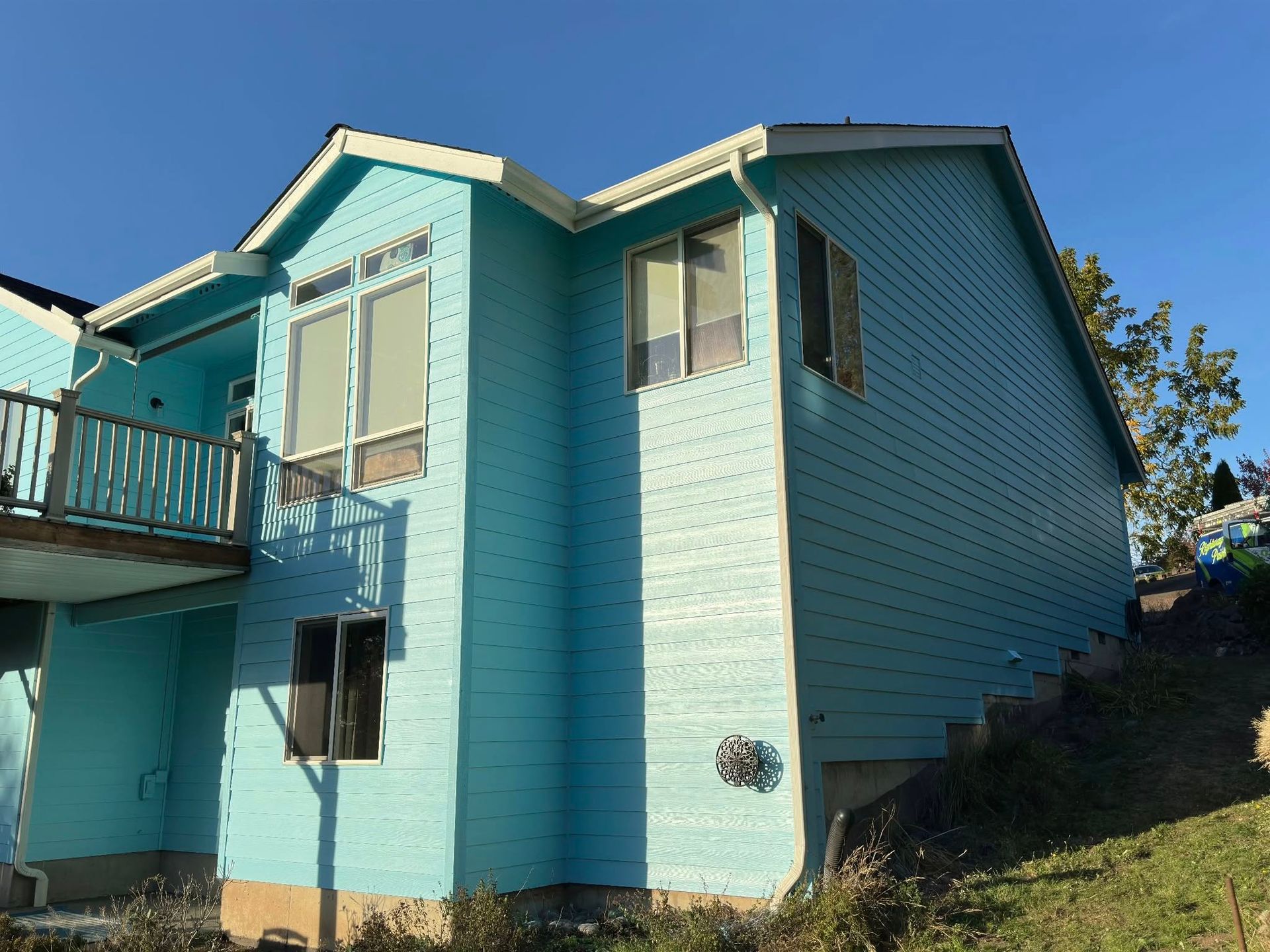 Blue-sided house with a deck and several windows against a clear, blue sky.