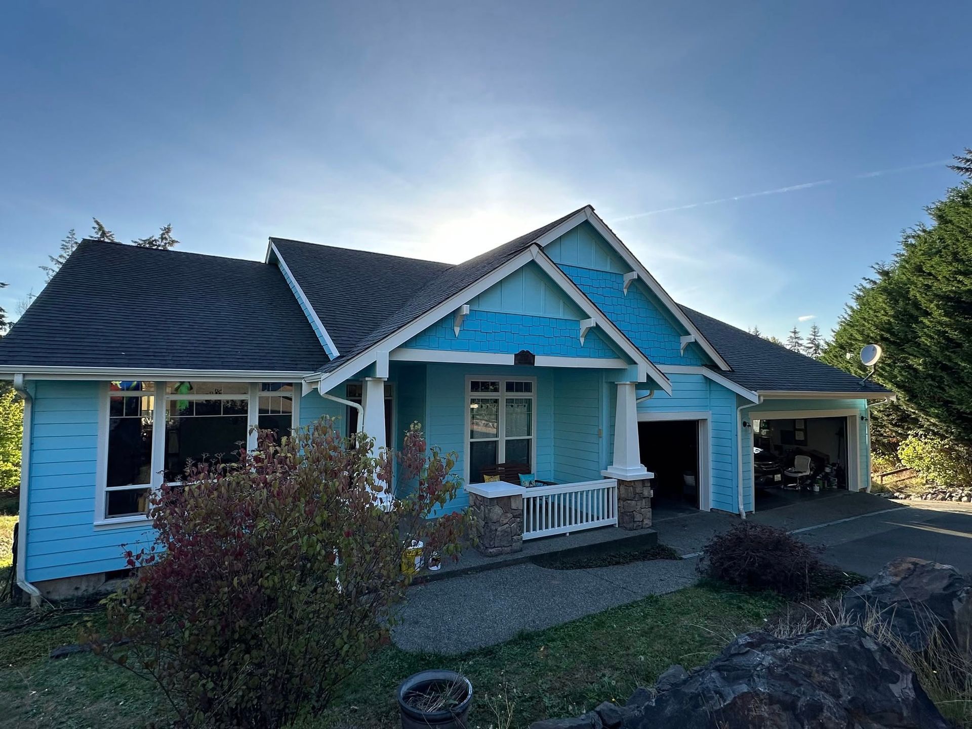 Blue house with a white porch and a garage on a sunny day.