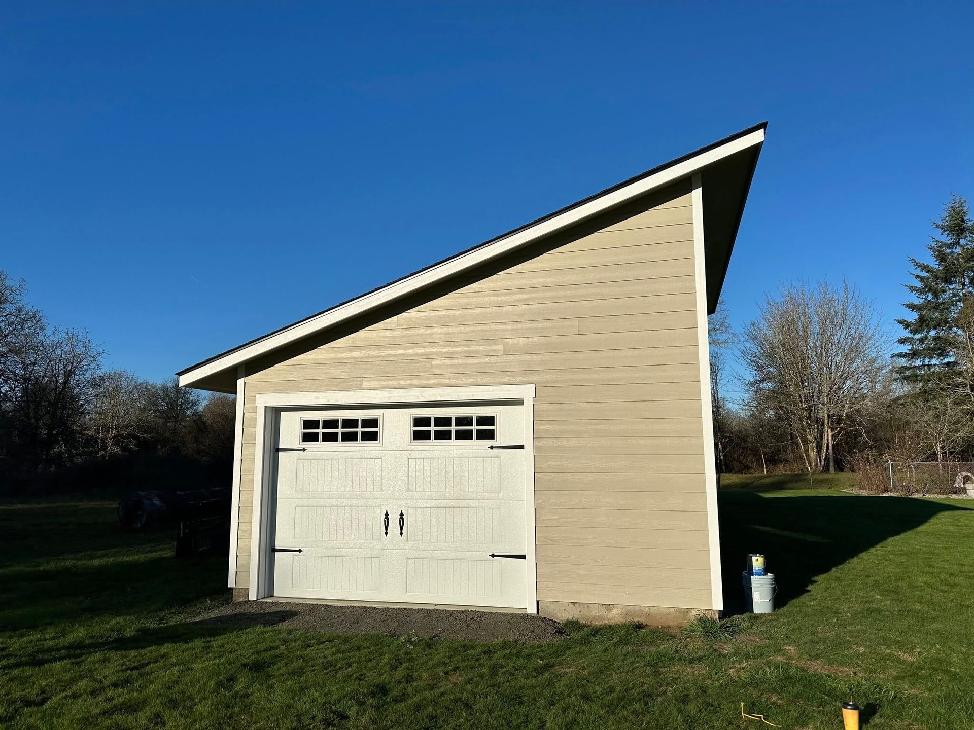 Tan garage with white door and slanted roof against blue sky.