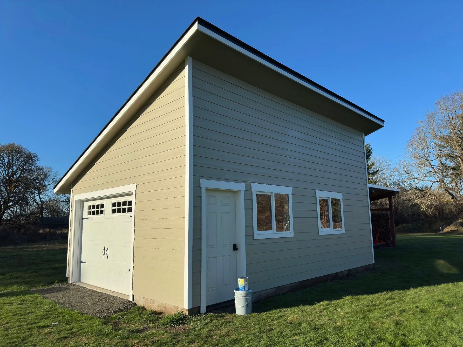 Tan garage with white trim and a white garage door, set in a grassy yard under a blue sky.