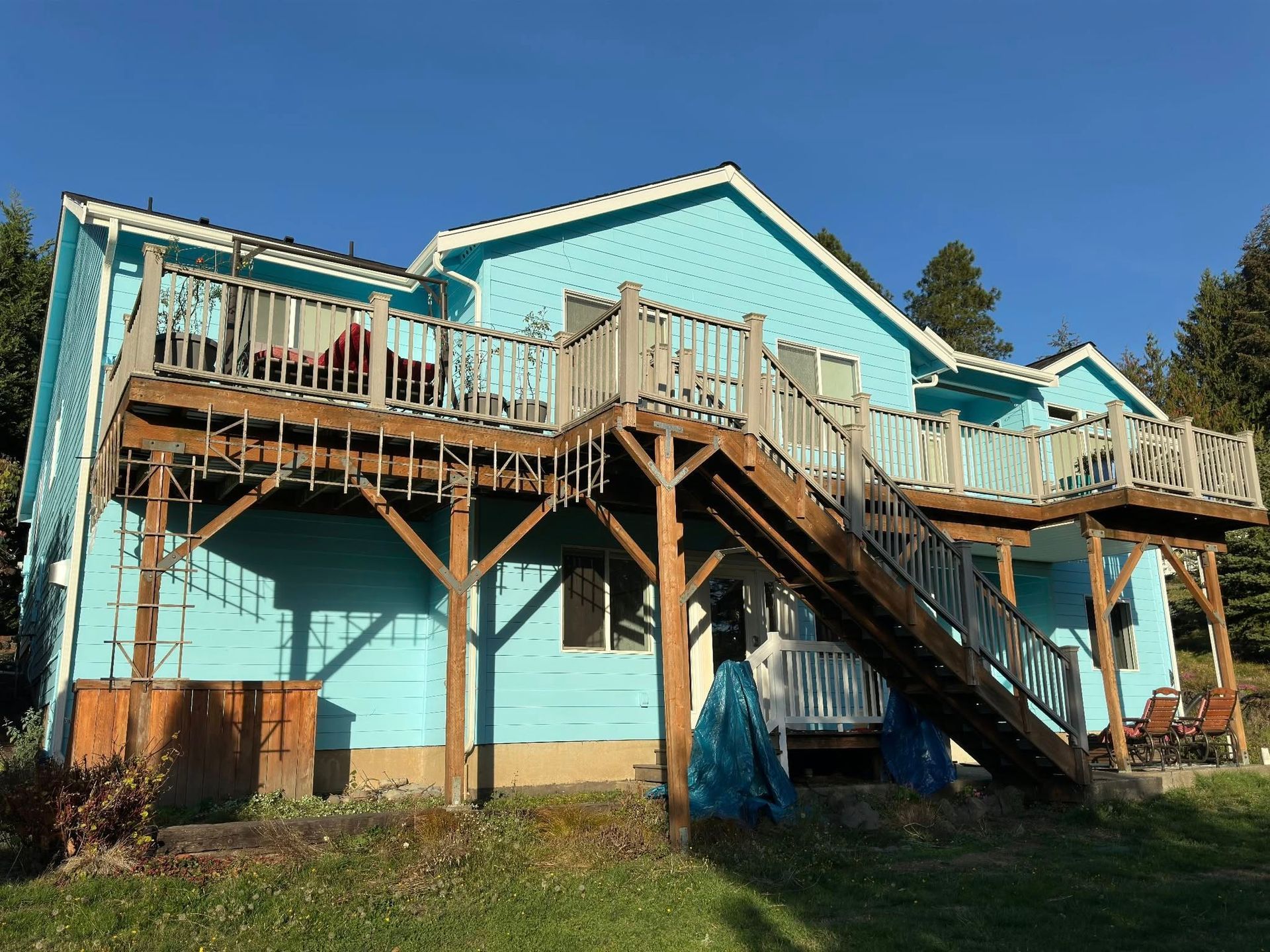Two-story blue house with wooden decks and stairs, set against a blue sky.