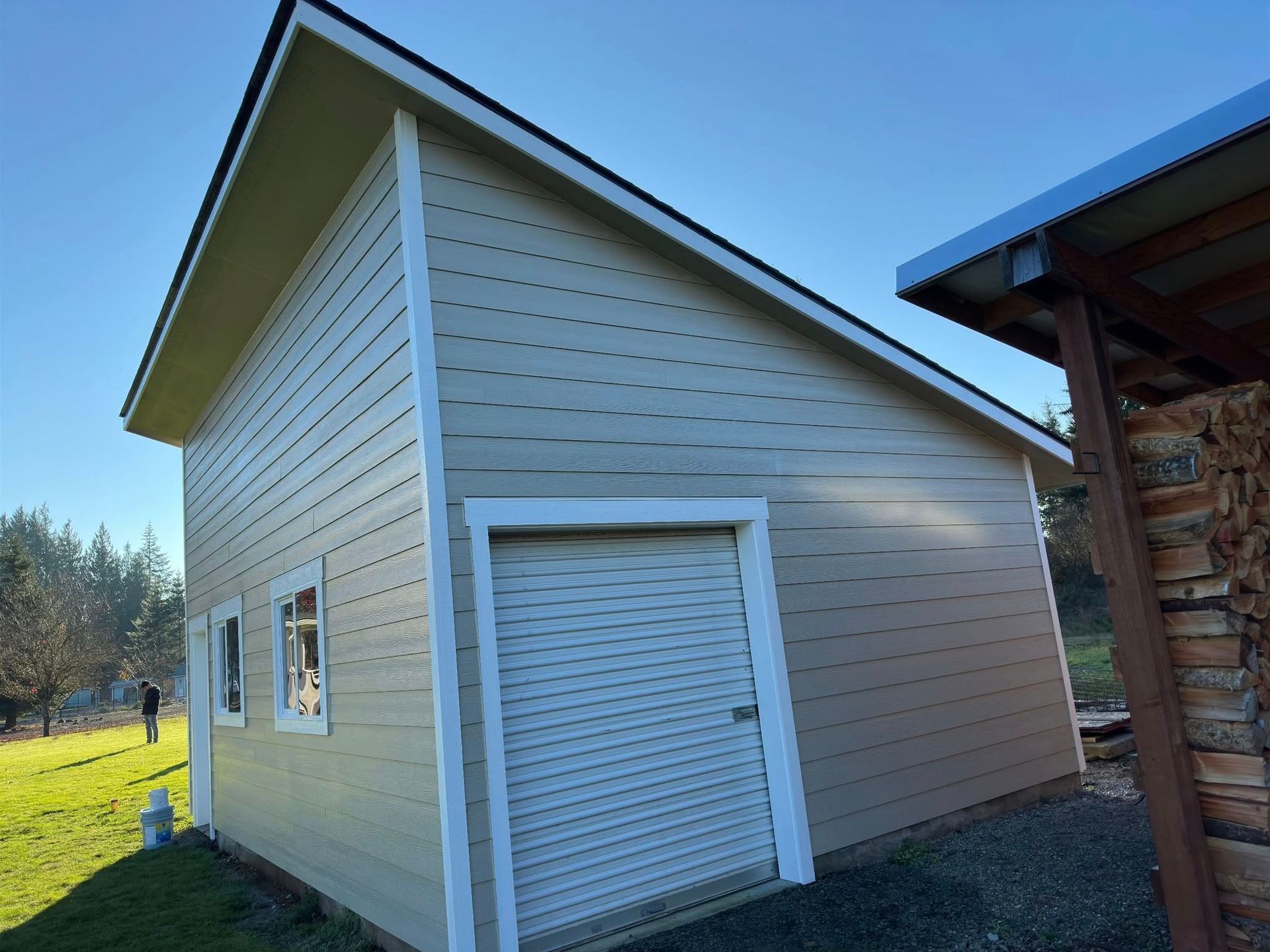 Beige shed with a roll-up door, white trim, and a sloped roof under a blue sky.