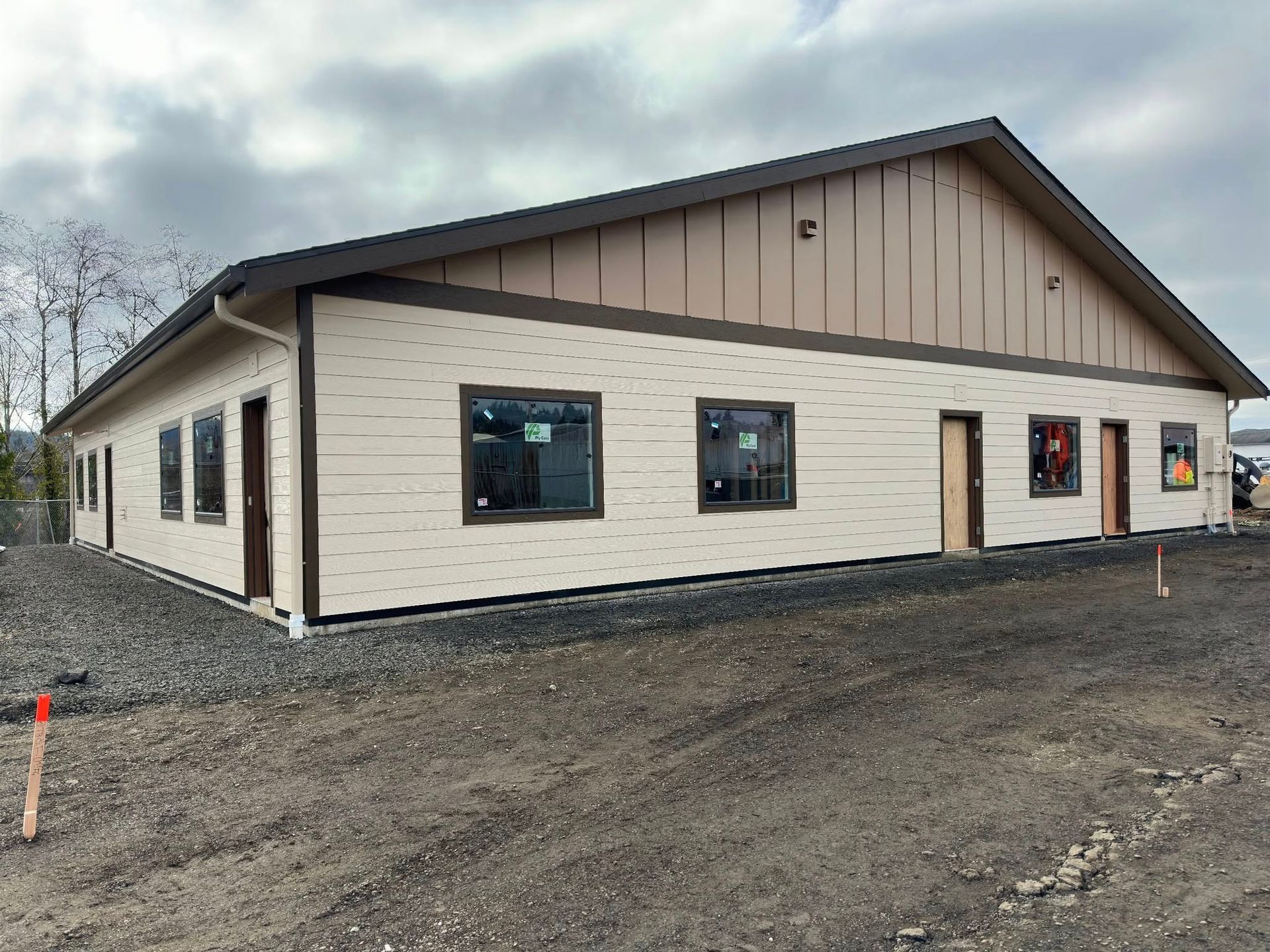 New commercial building under construction with tan siding and dark trim. Cloudy sky.