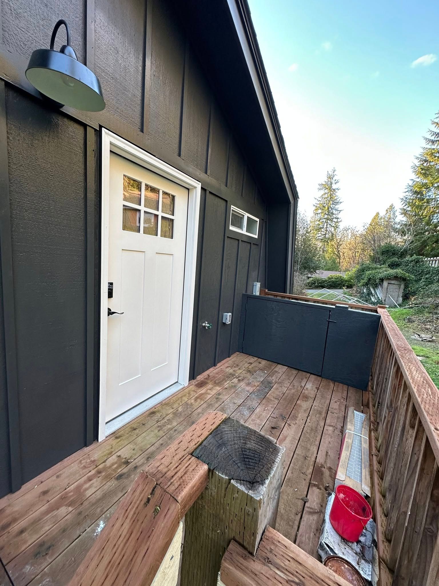 Exterior of a dark-painted building with a white door, deck, and black lantern.