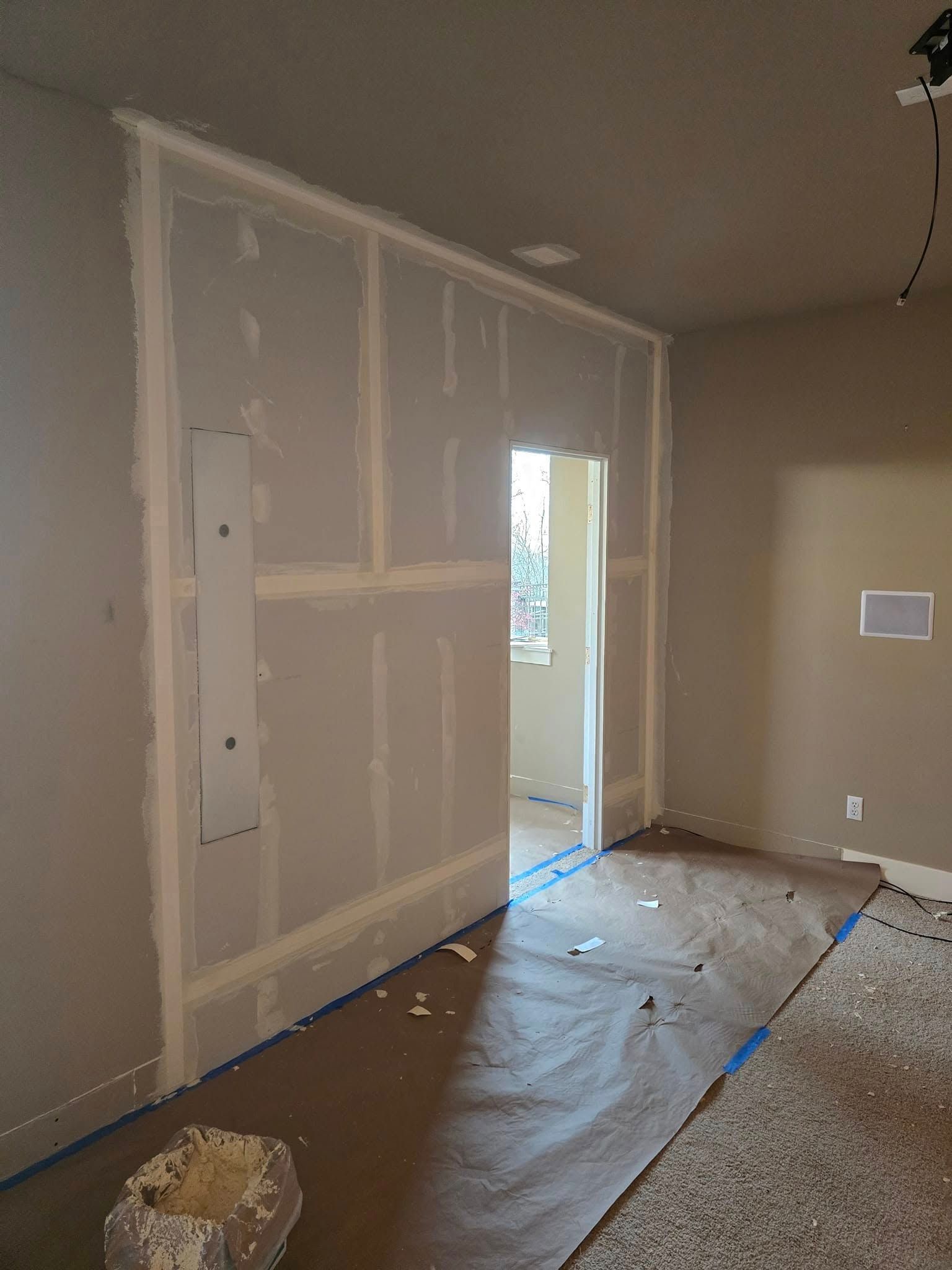 Room with partially finished drywall. Doorway in the middle, brown floor with paper covering.