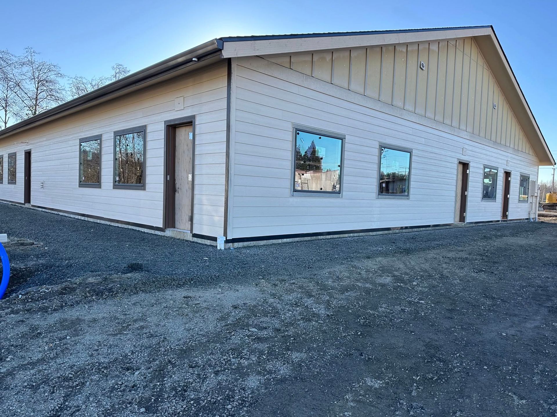 New commercial building with light siding, dark-framed windows, and a gravel lot.