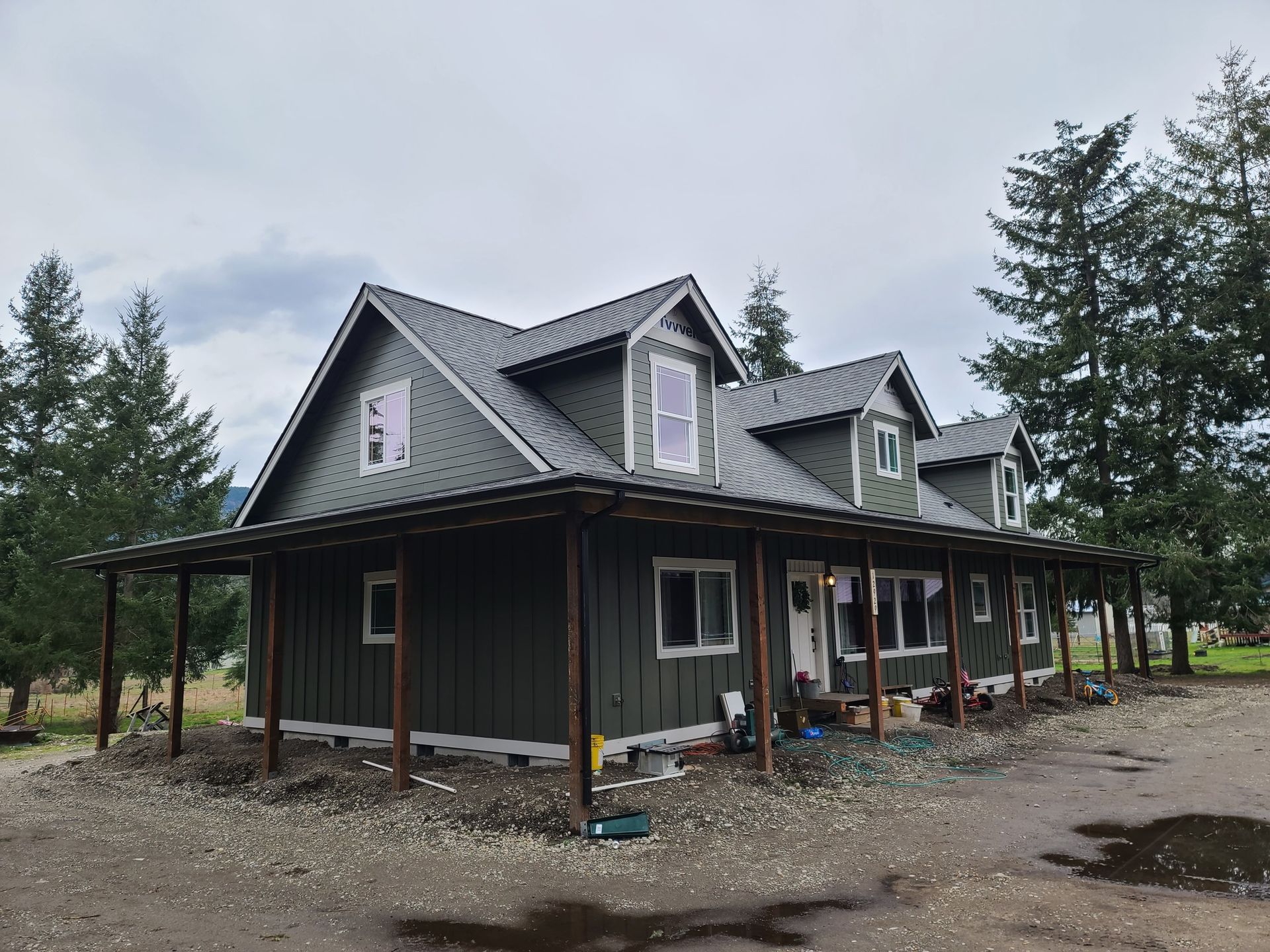 Green house with porch and gray roof against a cloudy sky.