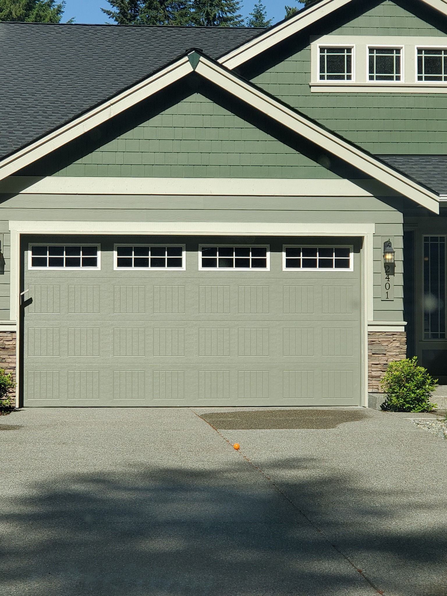 Green house with gray garage door and gravel driveway.