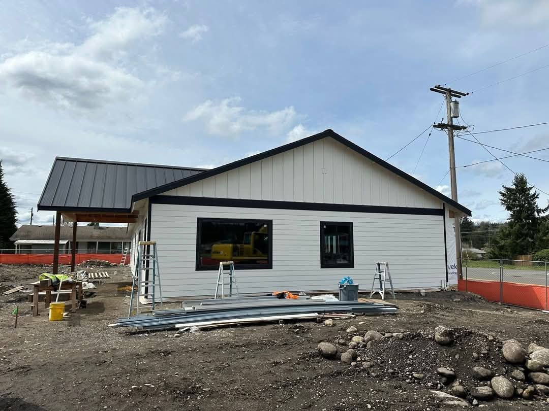 Construction of a small white house with a black roof and window frames. Construction materials are in the foreground.