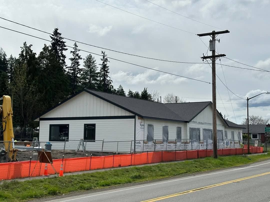 Construction site with a white building, black roof, and orange barrier along the road.