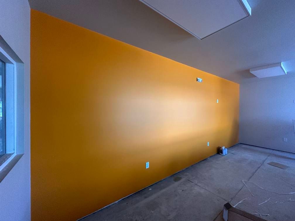 Yellow painted accent wall in a room, with electrical outlets, and a window.