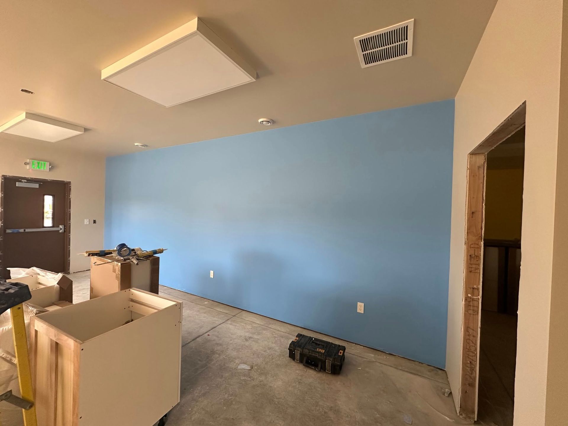 Interior room under construction, with blue accent wall, unfinished floor and cabinets, and rectangular lights.